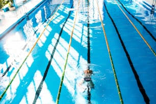 Hombre mayor nadando en una piscina cubierta. Jubilado activo disfrutando del deporte. Vista trasera y de ángulo alto.
