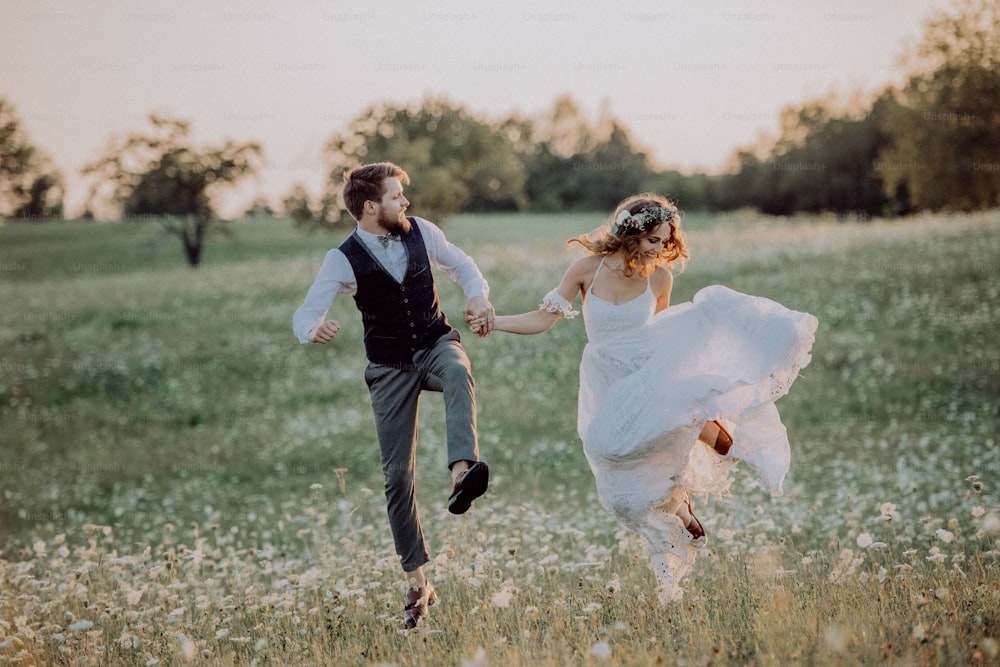 Beautiful young bride and groom outside in green nature at romantic sunset, holding hands, jumping high.