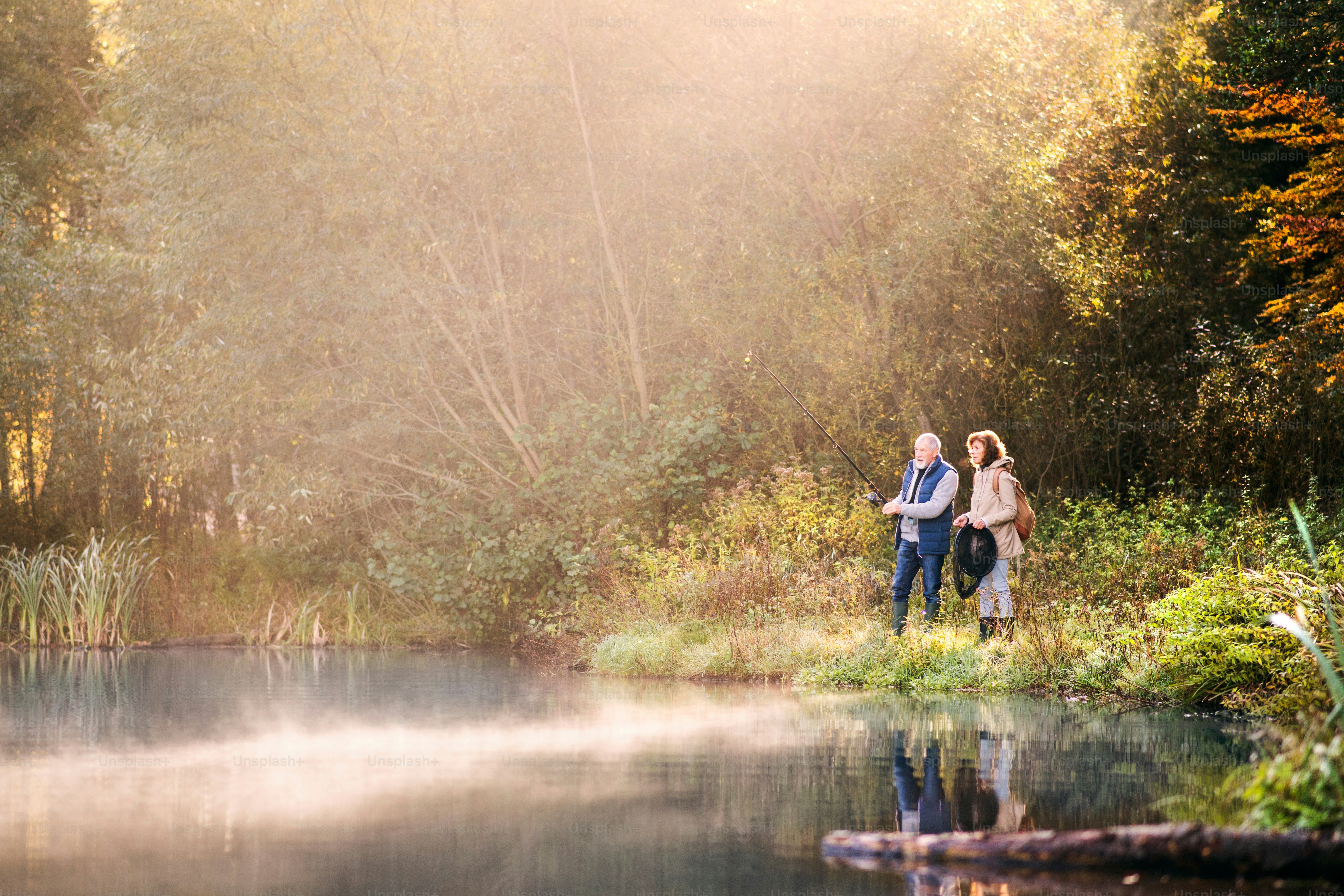 Aktives Seniorenpaar angelt am See. Eine Frau und ein Mann in einer wunderschönen Herbstnatur am frühen Morgen.