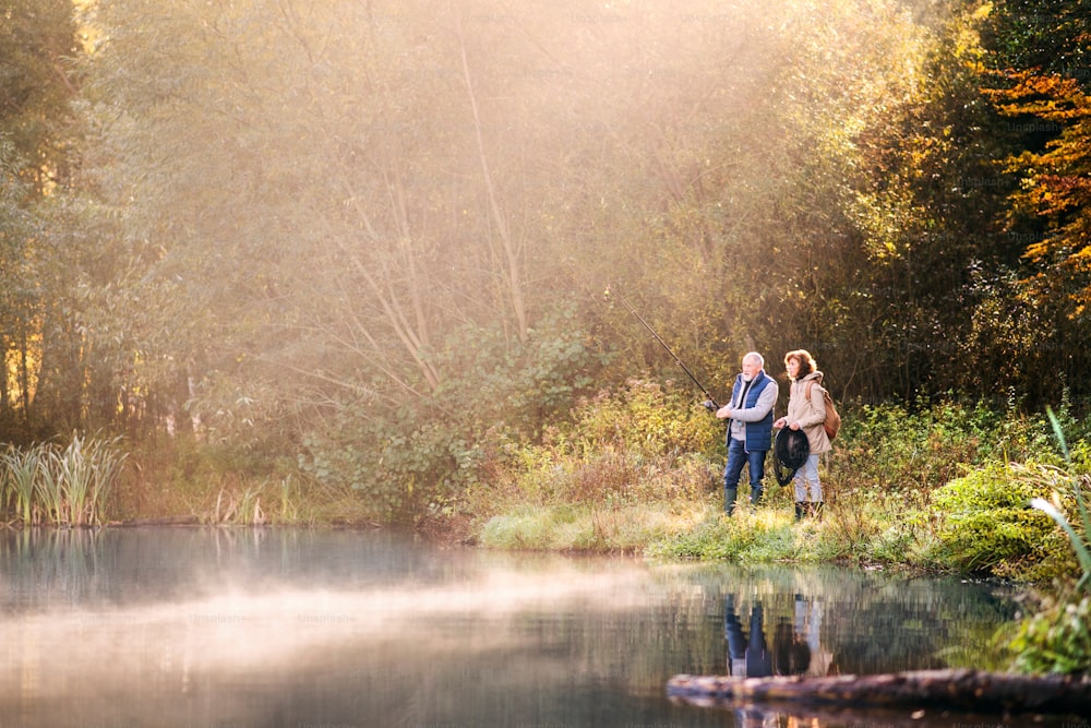 Active senior couple fishing at the lake. A woman and a man in a beautiful autumn nature in the early morning.
