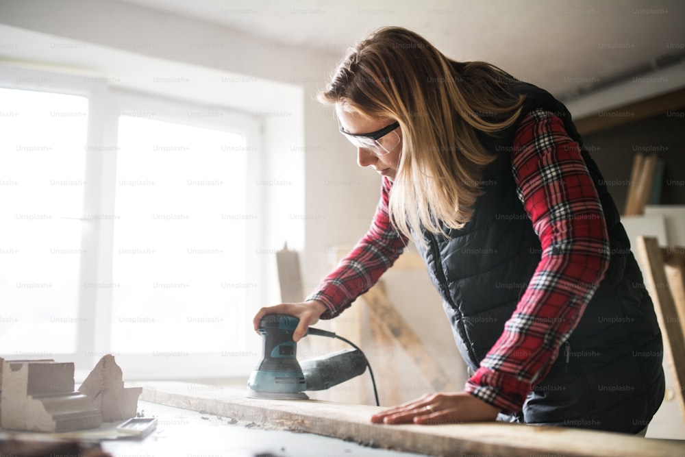Young woman worker in workroom. Female carpenter using a sander.