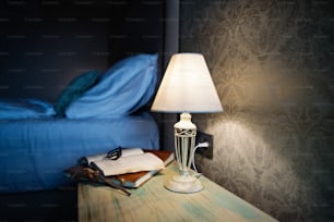 夕方のホテルの部屋。ホテルの部屋のベッド横のベッドサイドテーブルで点灯するベッドサイドランプ。