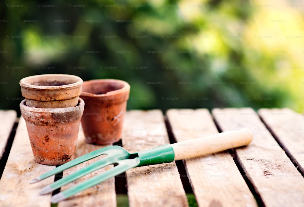 Close up of garden tools in the garden. Hand fork and flower pots on the wooden table.