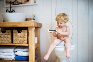 Cute toddler with a smartphone in the bathroom. Little boy sitting on the toilet.
