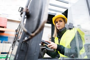 Female forklift truck driver in an industrial area. A woman sitting in the fork lift outside a warehouse.