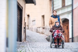Vater im Rollstuhl und kleiner Sohn auf einem Spaziergang. Ein Betreuer, der behinderten älteren Mann hilft.
