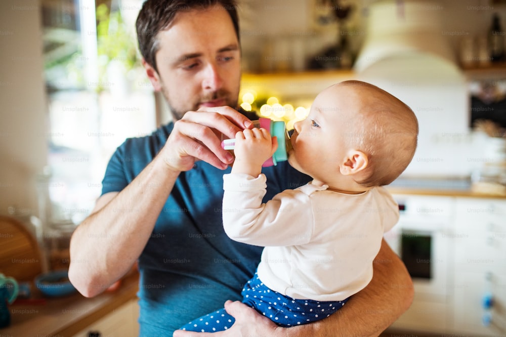 Un padre con una hija pequeña en casa. Una linda chica bebiendo agua de la botella. Paternidad.