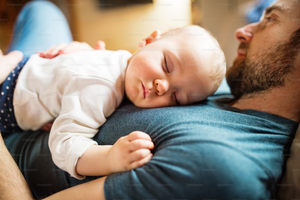 家で女の赤ちゃんを連れた父親が、ソファで寝ている。育児休暇。クローズアップ。
