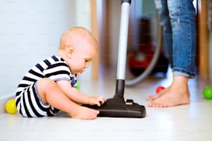 Unrecognizable young mother with a baby son doing housework. Beautiful woman and baby boy hoovering.
