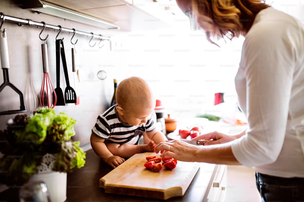 Mãe jovem irreconhecível com um filho bebê fazendo tarefas domésticas. Mulher bonita e menino cozinhando na cozinha.