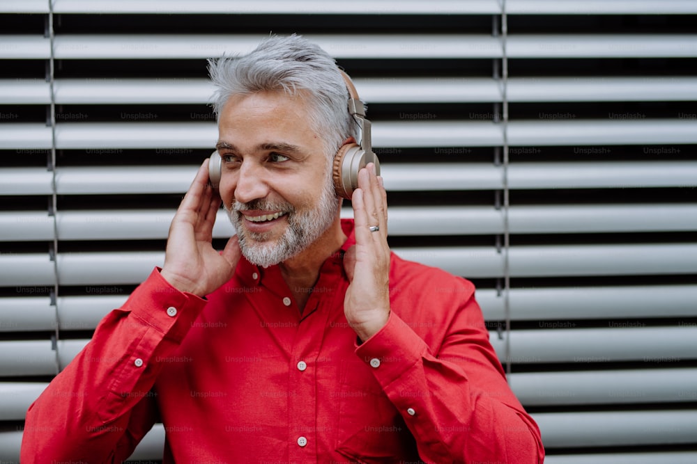 A mature businessman enjoying music in headphones relaxing on balcony during break at work.