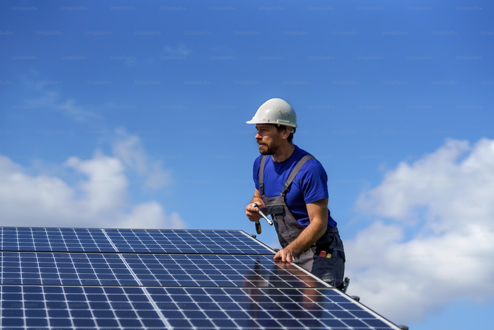 A man worker installing solar photovoltaic panels on roof, alternative energy concept.