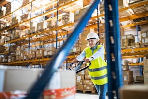 A senior woman warehouse worker or supervisor pulling a pallet truck with boxes.