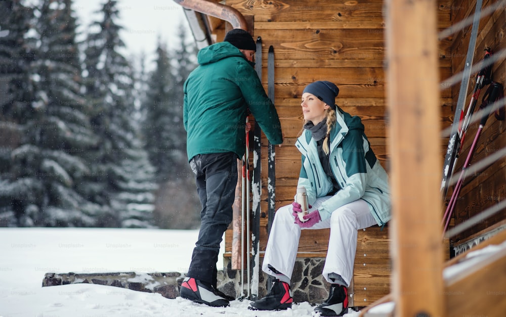Mature couple resting by a wooden hut outdoors in winter nature, cross country skiing.