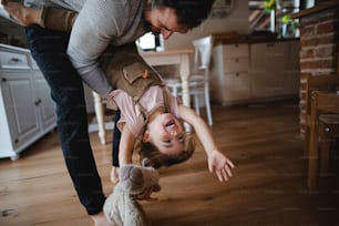 Un padre maturo con una figlia piccola che gioca in casa in casa, tenendola a testa in giù.