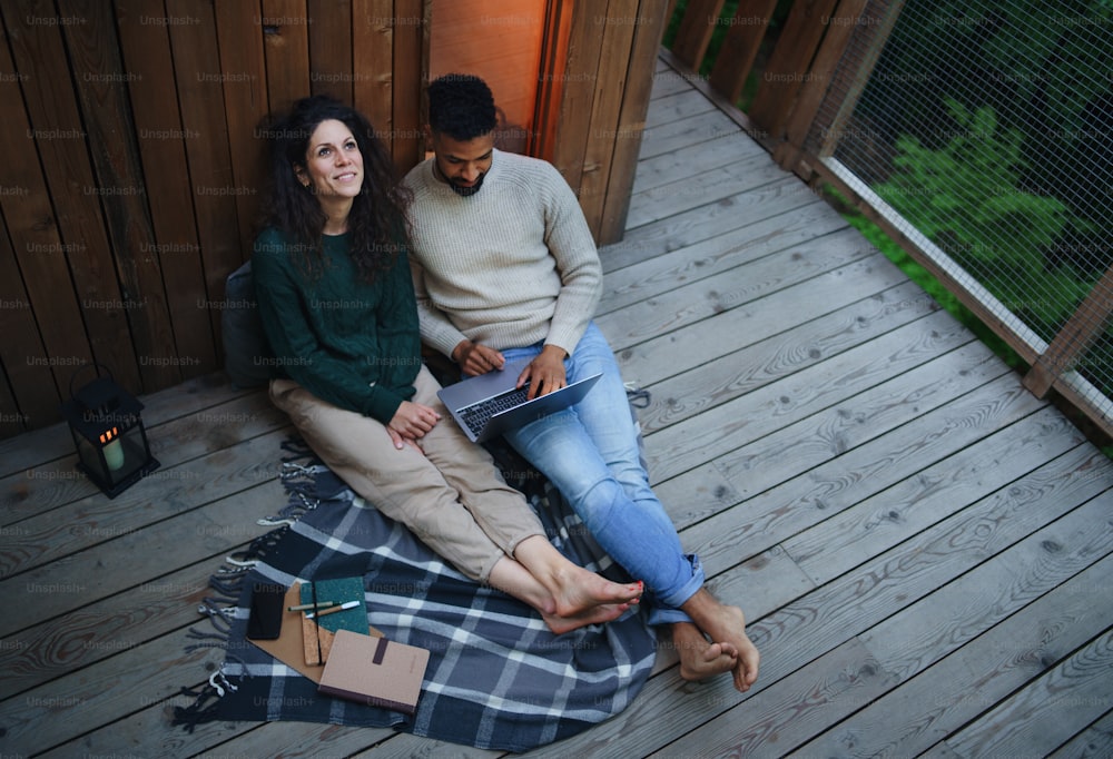 A top view of happy couple with laptop resting outdoors in a tree house, weekend away and remote office concept.