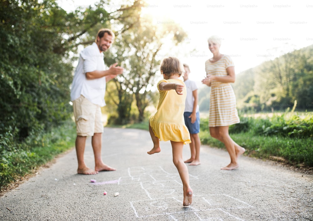Uma jovem família com crianças pequenas brincando de amarelinha em uma estrada no campo no verão.