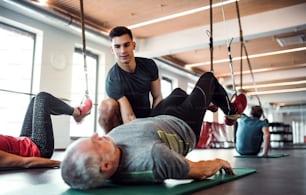 A group of cheerful seniors in gym with a young personal trainer doing exercise with TRX.