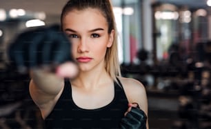 Una vista frontal de una niña o mujer joven con guantes, haciendo ejercicio en un gimnasio.
