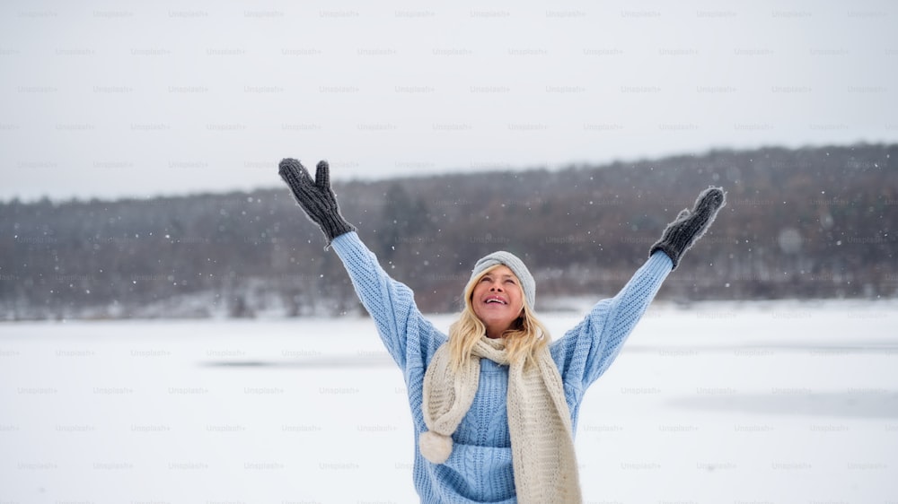Front view portrait of happy senior woman outdoors standing in snowy nature, stretching arms.