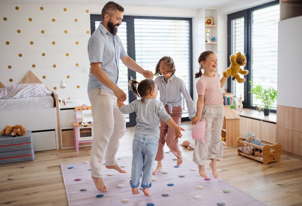 A father with three daughters indoors at home, playing on floor and jumping.