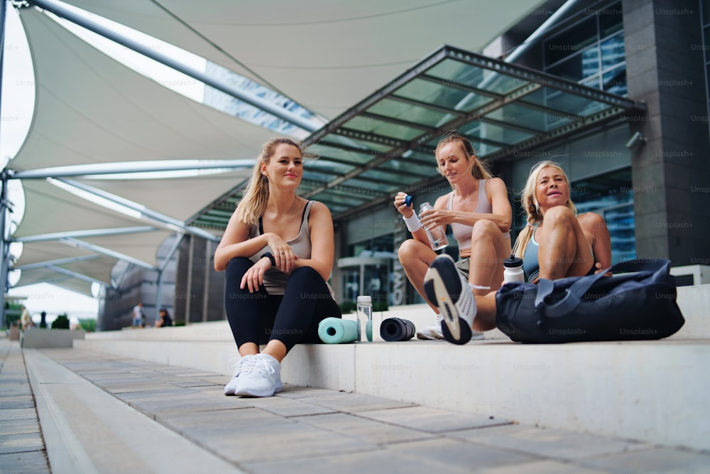 Un gruppo di donne giovani e anziane sedute dopo l'esercizio all'aperto in città, parlando.