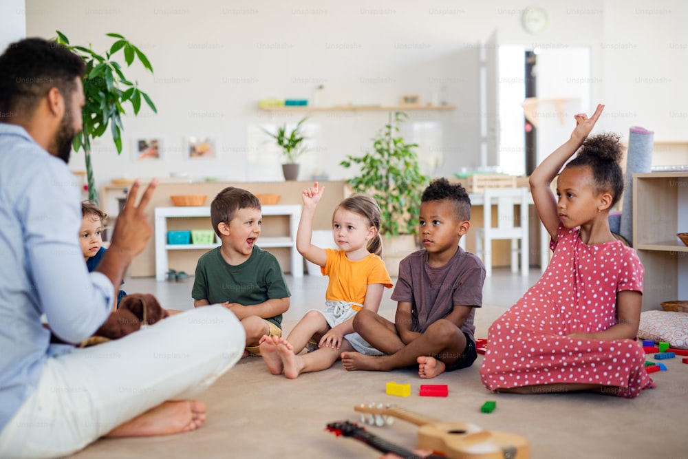 Um grupo de pequenas crianças da creche sentadas no chão dentro de casa de aula.
