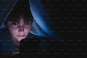 Teen girl using a smartphone, hiding under blanket at nigh, social networks cocnept.