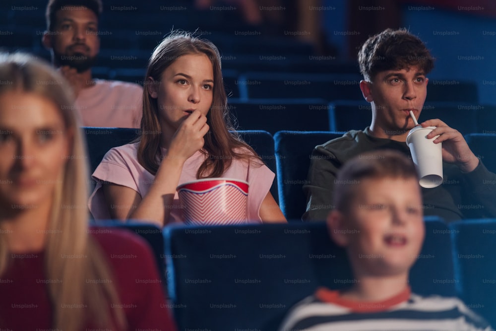A front view of cheerful young couple with drink and popcorn in the cinema, watching film.