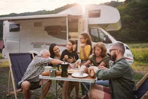 Una famiglia multigenerazionale seduta e mangia all'aperto in auto, viaggio di vacanza in roulotte.