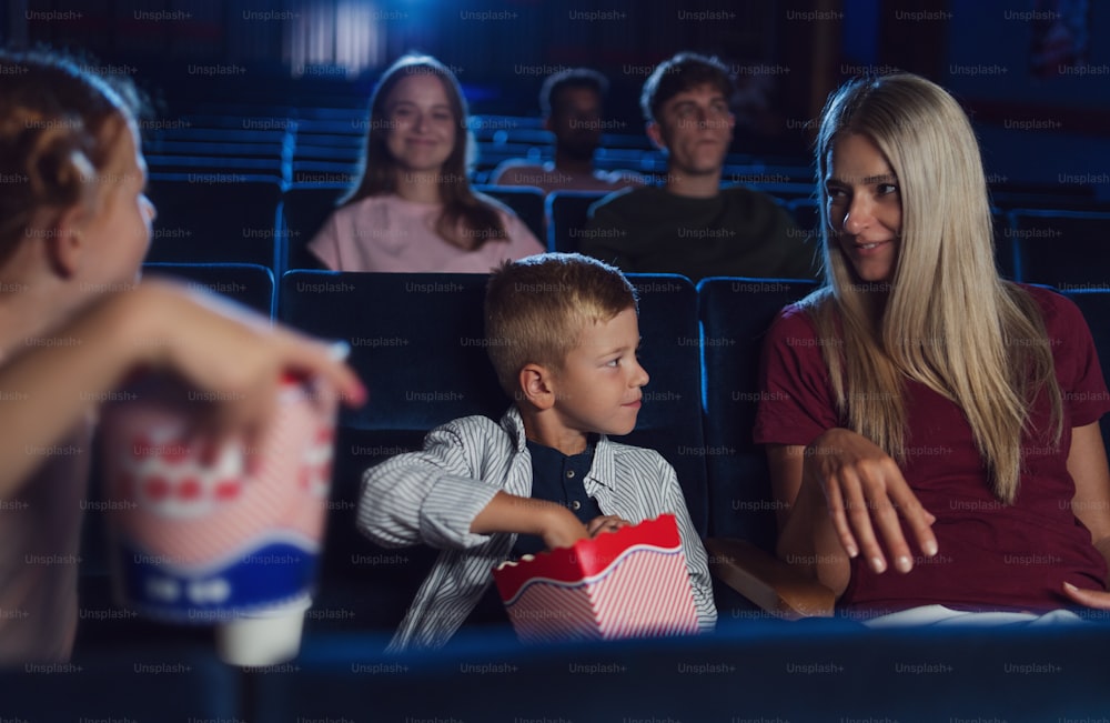 A mother with happy small children in the cinema, watching film and eating popcorn.