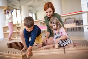 Group of small nursery school children with teacher sitting on floor indoors in classroom, montessori learning concept.