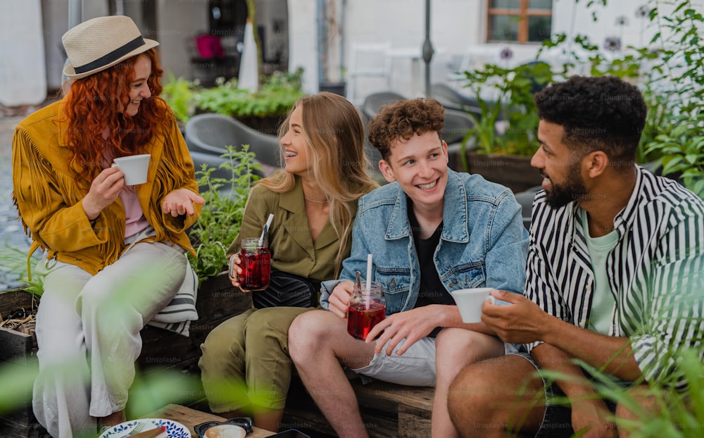 Un grupo de jóvenes felices sentados en un café al aire libre en un viaje por la ciudad, hablando.