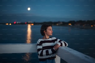 Um retrato de menina pré-adolescente olhando para o lado ao ar livre no cais pelo mar ao entardecer.