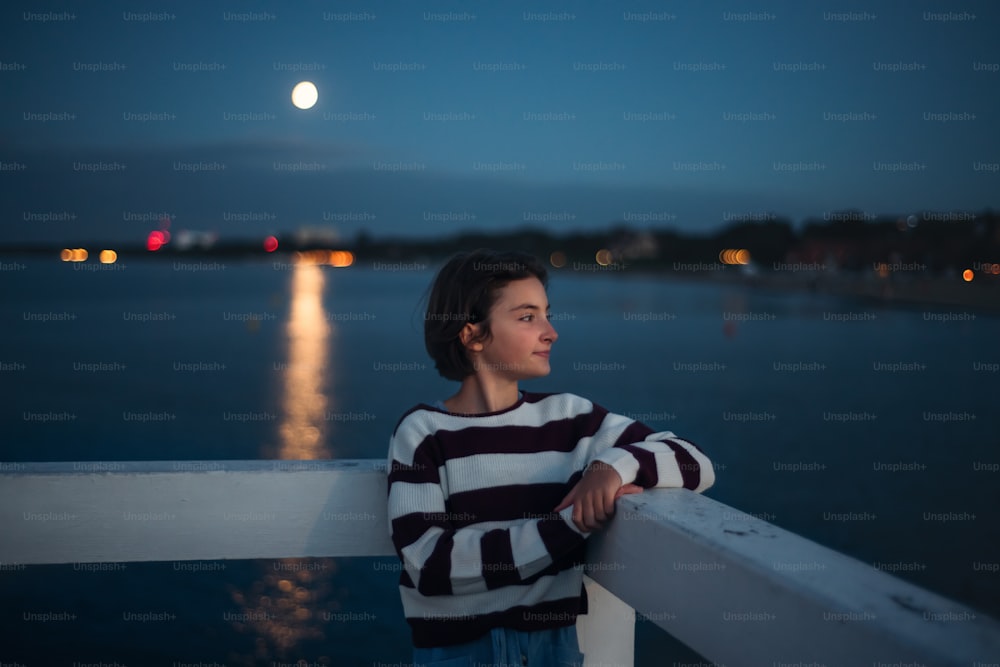 A portrait of preteen girl looking aside outdoors on pier by sea at dusk.