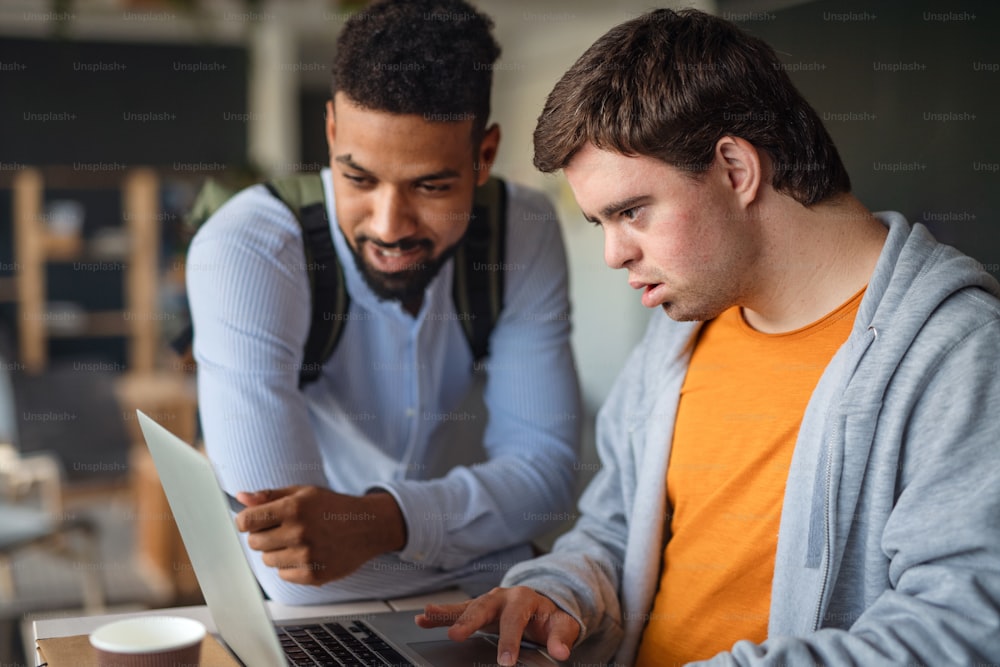 A young man with Down syndrome and his tutor using lapotp indoors at school.