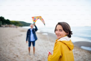 A senior man and his preteen granddaughter playing with kite on sandy beach.