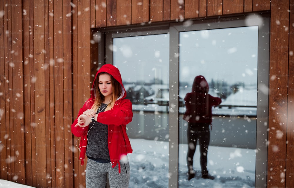 A portrait of young girl or woman with earphones using smartwatch outdoors in winter.