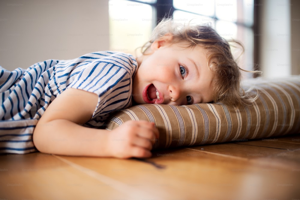 A happy toddler girl lying on the floor indoors at home, playing.