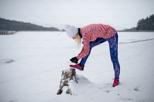 Vue latérale d’une femme âgée active à l’extérieur en hiver enneigé, nouant des lacets.