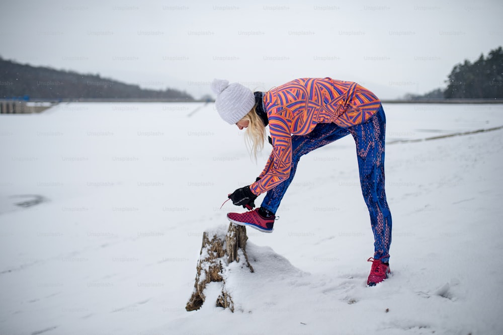 Vista laterale della donna anziana attiva all'aperto nell'inverno nevoso, legando i lacci.