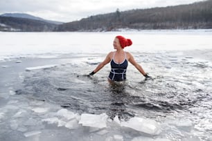 Una vista frontal de una mujer mayor activa en traje de baño al aire libre en invierno, concepto de terapia de frío.