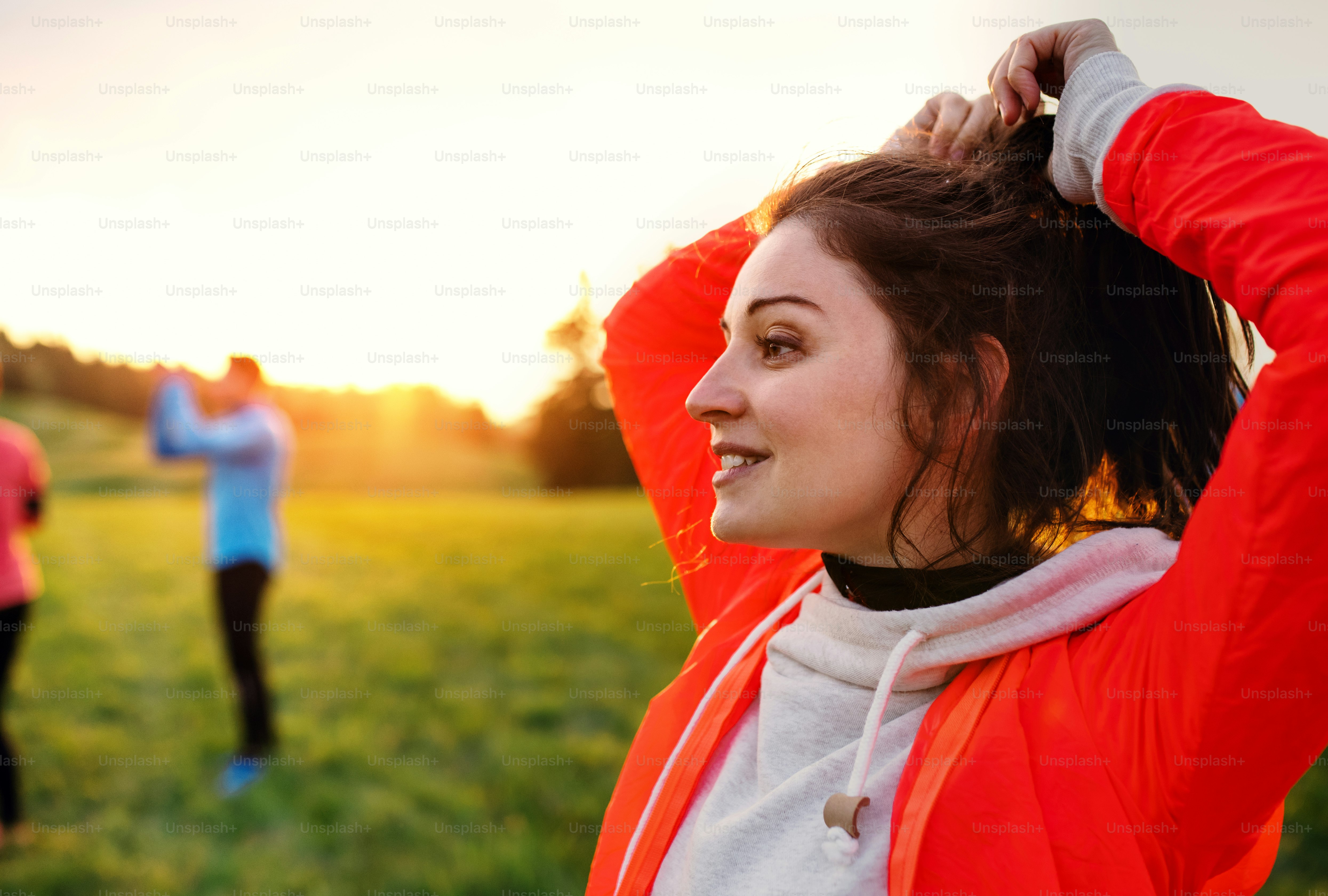 A portrait of young woman with group of people doing exercise in nature, resting.