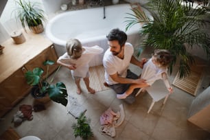 A top view of mature father with two small children indoors at home, getting ready for a bath.