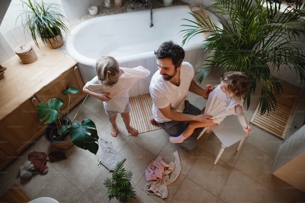 A top view of mature father with two small children indoors at home, getting ready for a bath.