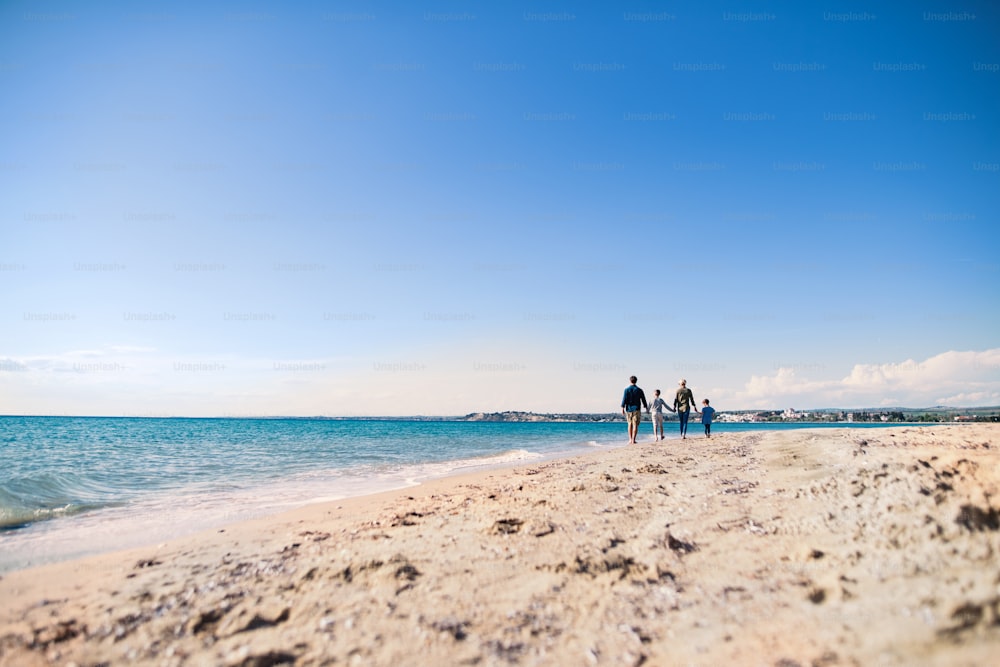 Rückansicht der jungen Familie mit zwei kleinen Kindern, die barfuß draußen am Strand laufen. Kopierbereich.,