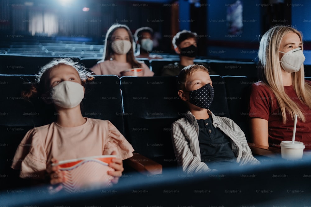 A mother with happy small children watching film in the cinema, coronavirus concept.