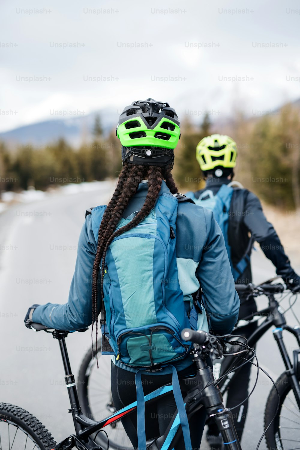 A rear view of two mountain bikers on road outdoors in winter.