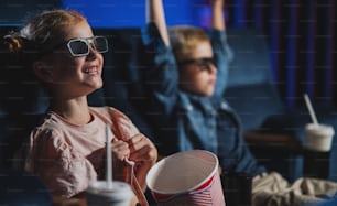 Small children with 3d glasses and popcorn in the cinema, watching a film.