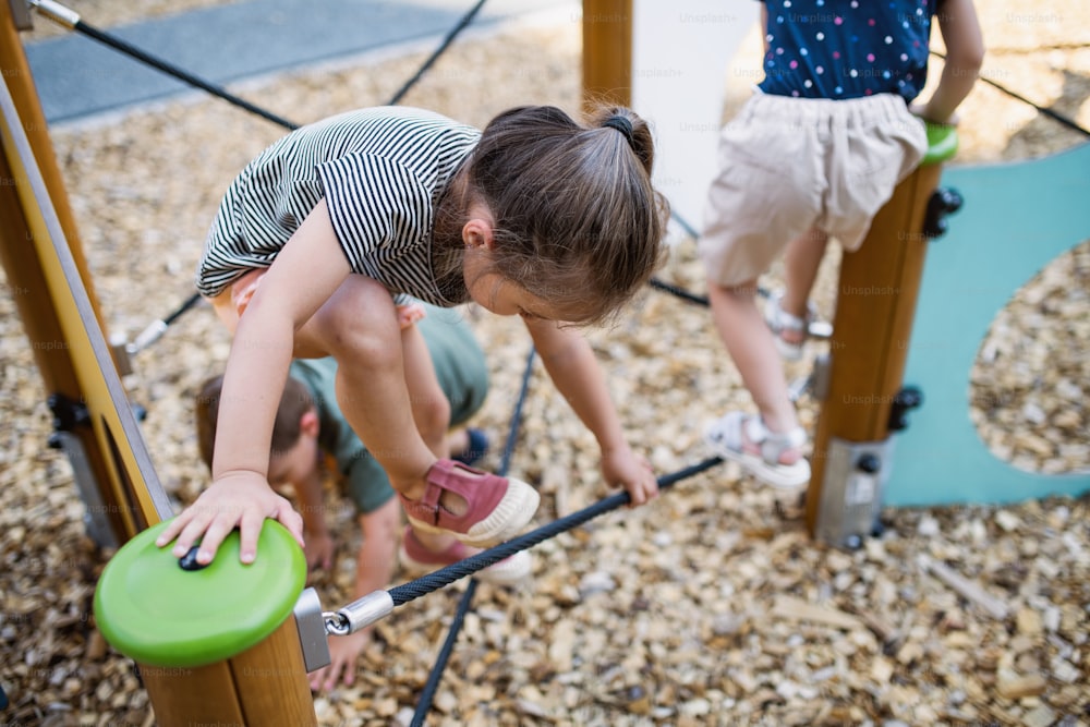 A group of small nursery school children playing outdoors on playground, climbing.